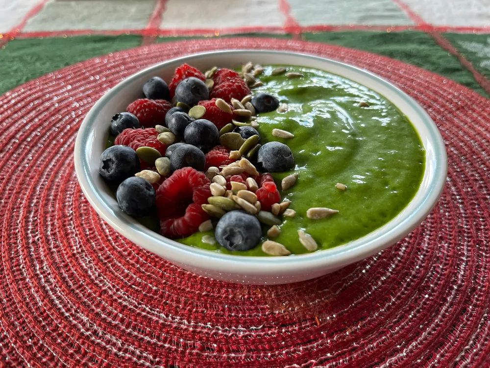 A green smoothie bowl topped with blueberries, raspberries and pumpkin seeds