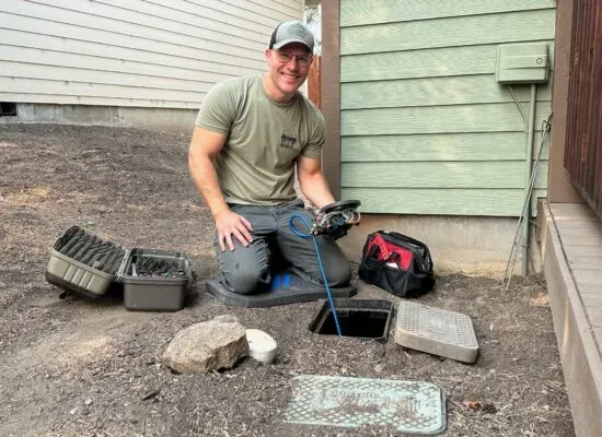 An irrigation tech kneeling at an open valve box next to a house in Bend