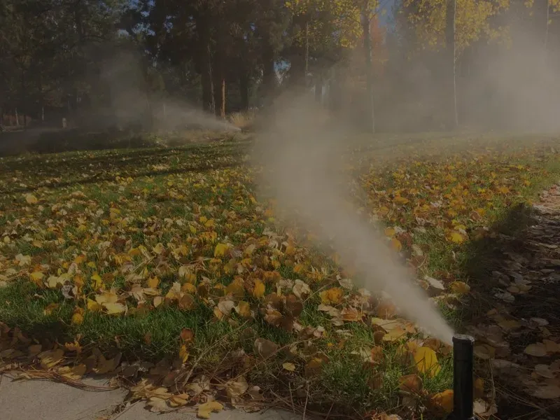 Air and mist blowing out of a sprinkler head on a fall lawn covered in leaves