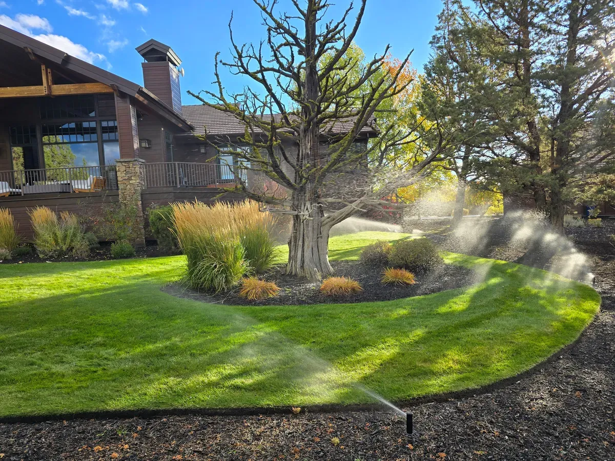 Sprinklers running on a green lawn in front of a Bend home