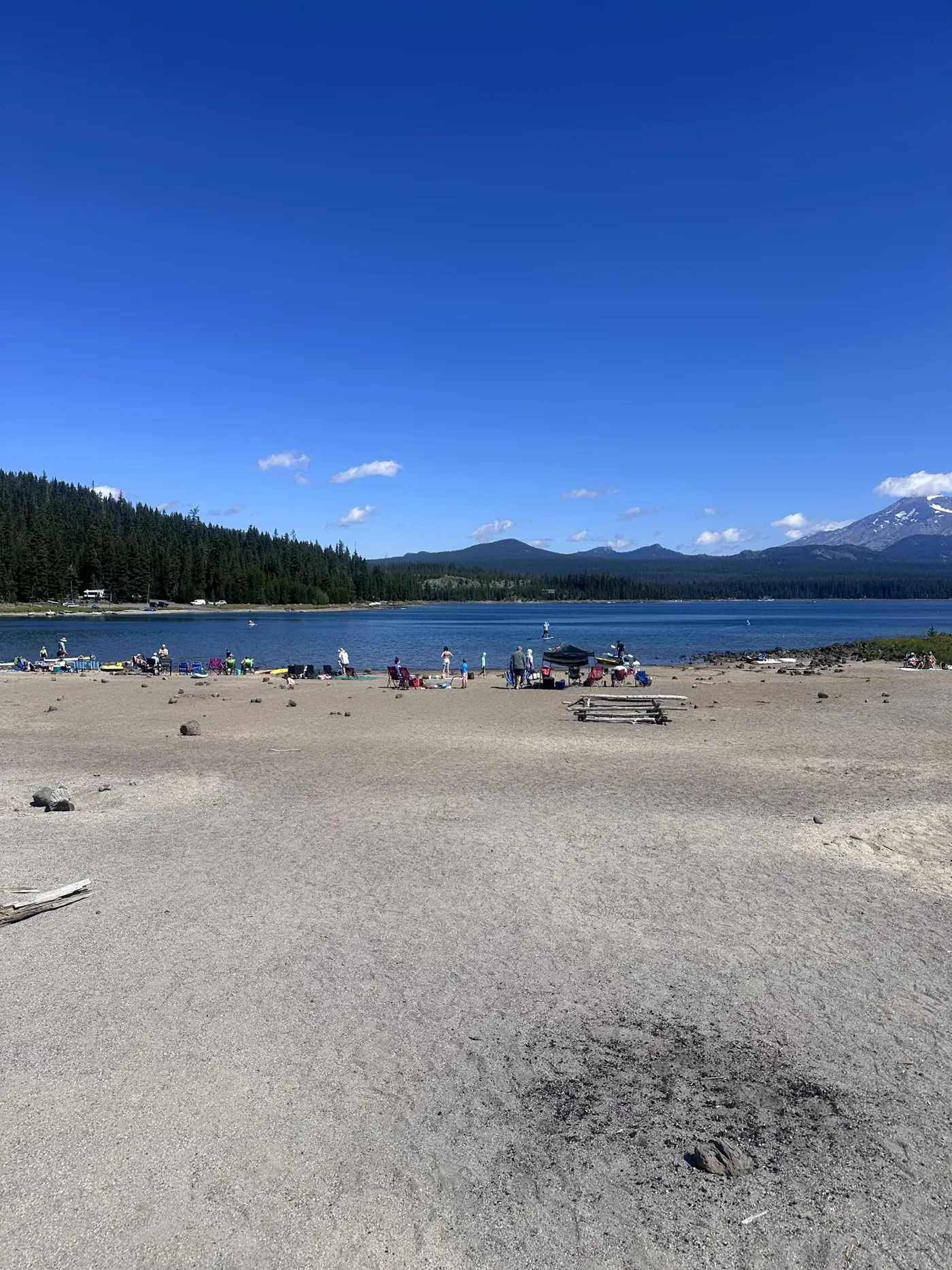 A sandy beach with people at a Cascade lake with a snowcapped peak behind