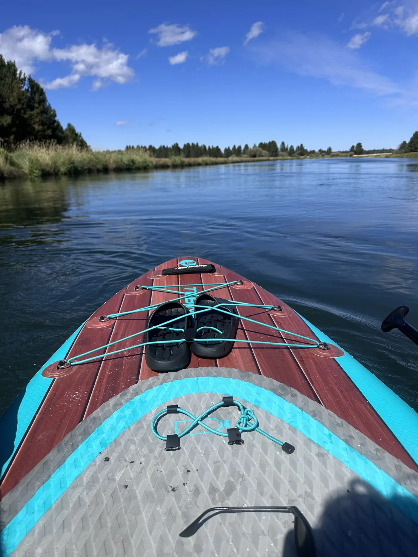 The nose of a paddleboard on a calm stretch of river under blue sky