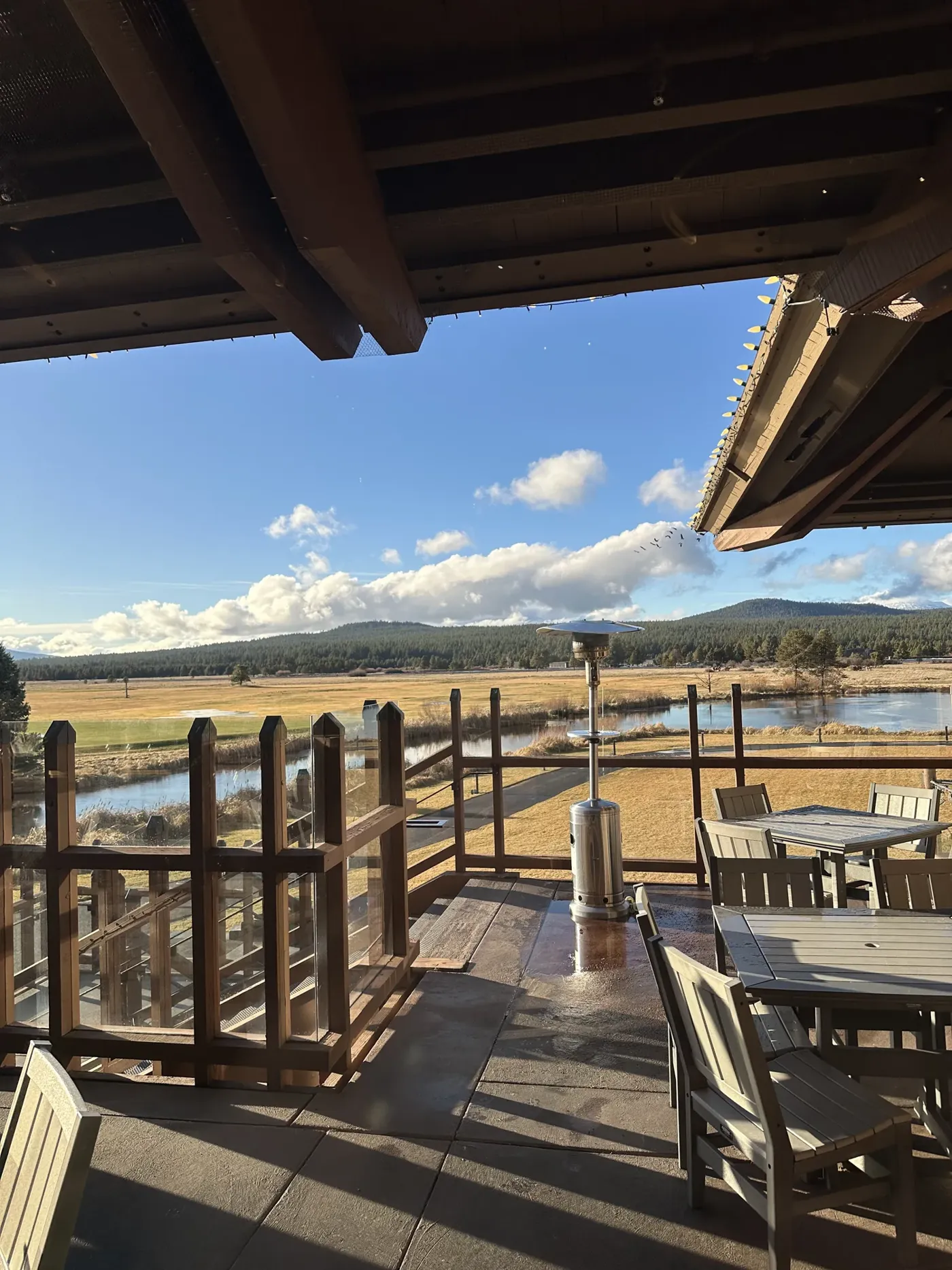 A covered wooden deck with tables overlooking a meadow and mountains