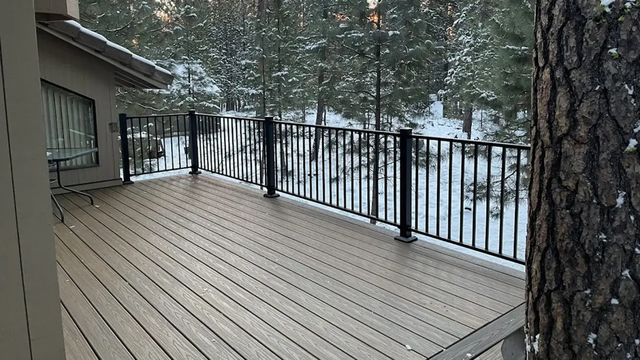 A new gray composite deck with black metal railing among snowy ponderosa pines