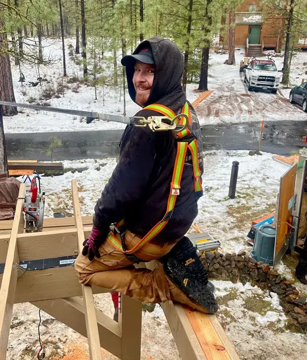 A deck builder in a safety harness working on a new deck frame in snow