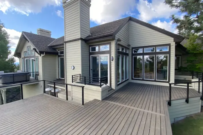 A large gray composite deck with black cable railing and a hot tub behind a tan two-story house