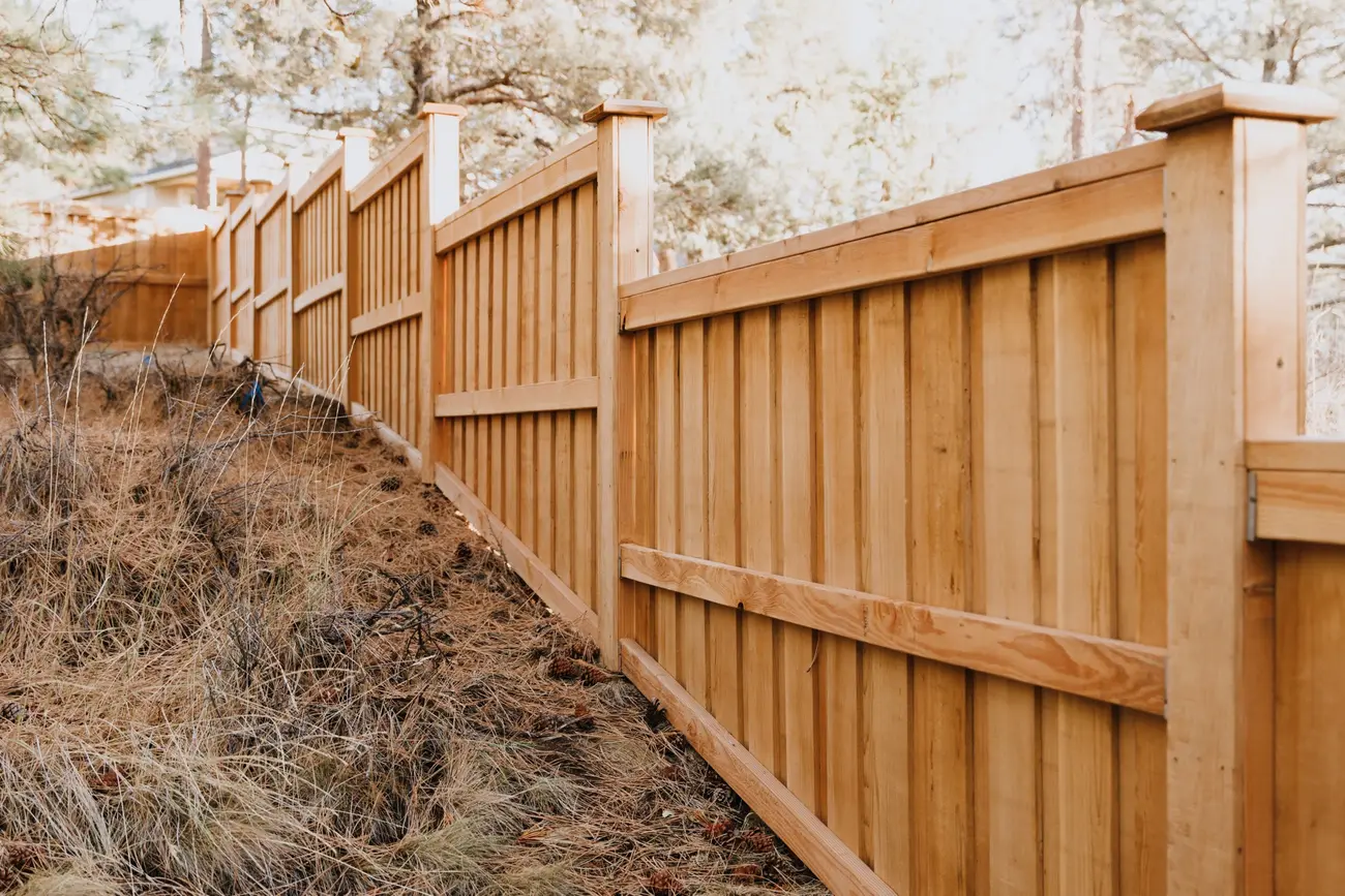 A new cedar privacy fence with a top cap stepping down a slope through pine needles