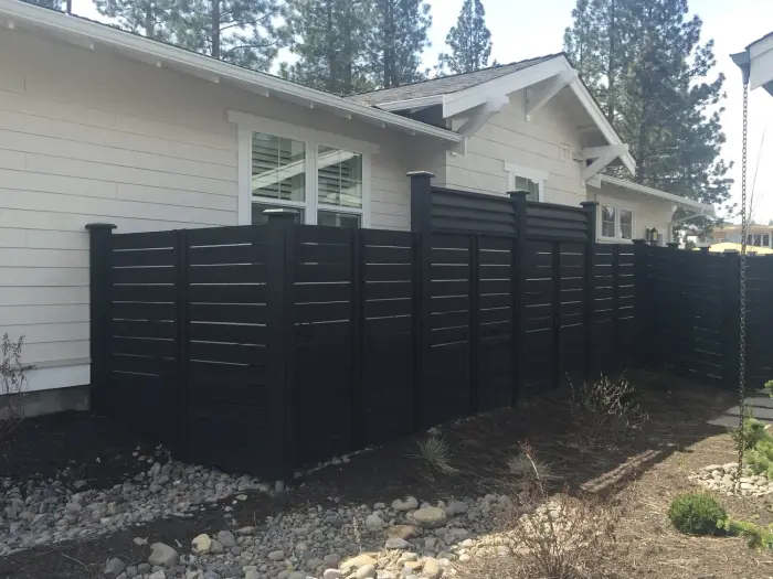 A black horizontal-board privacy fence beside a white craftsman house