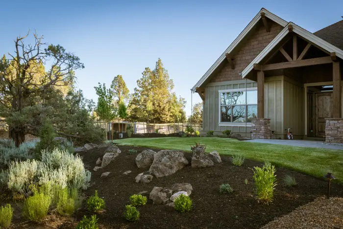 A newly planted east Bend yard with ornamental grasses, boulders and fresh bark around a lawn and a craftsman house