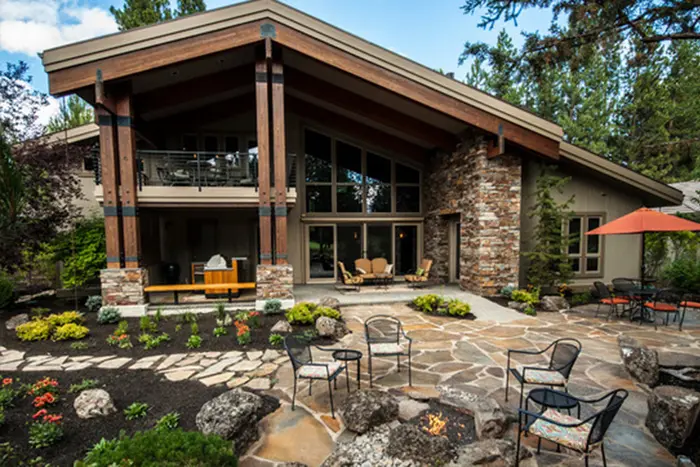 A flagstone patio with outdoor chairs and low-water plantings behind a stone-and-timber house in Broken Top